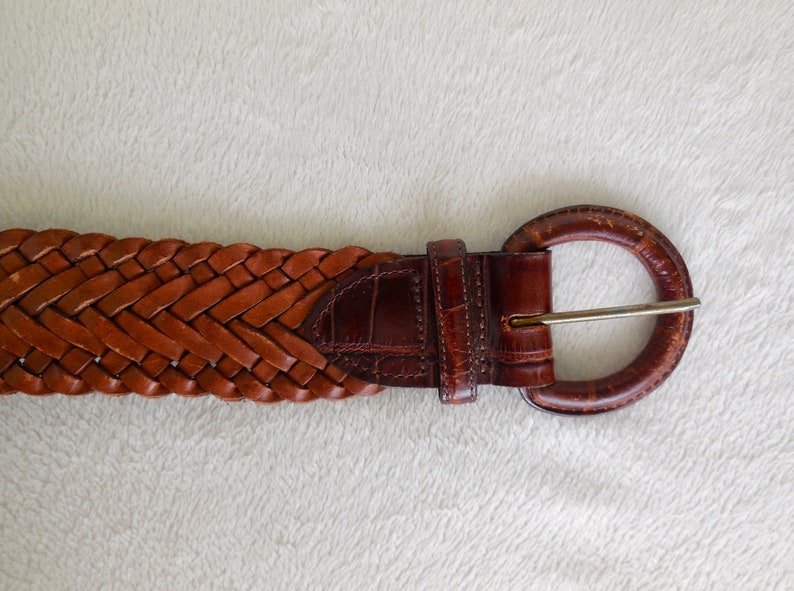 May include: A brown leather belt with a braided design and a round buckle.