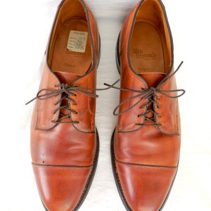 May include: A pair of brown leather Allen Edmonds Margate dress shoes, viewed from above. The shoes have a classic cap-toe design with brown laces and a dark brown sole. The interior of the shoe is tan.