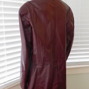 May include: A burgundy leather jacket with a long, fitted style. The jacket has a collar and a button closure.