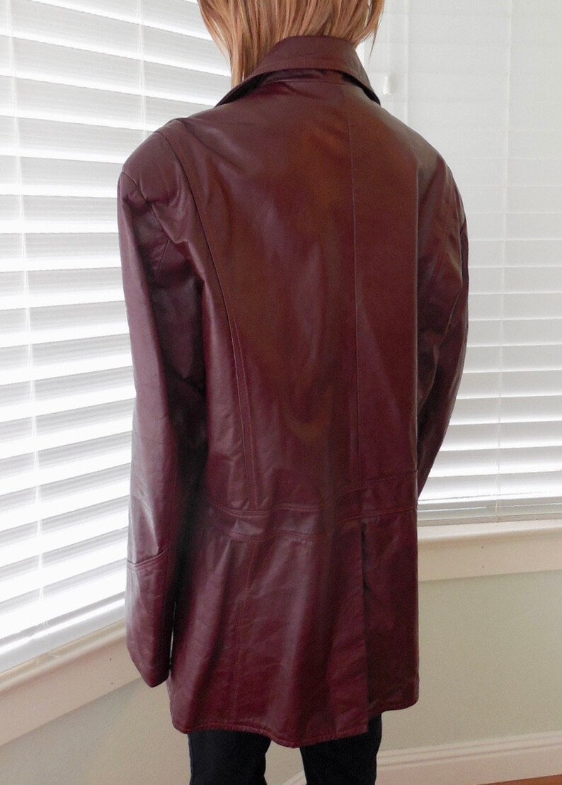 May include: A burgundy leather jacket with a long, fitted style. The jacket has a collar and a button closure.