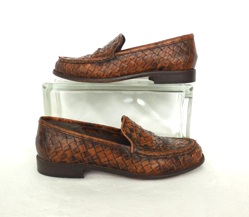 May include: A pair of brown leather woven loafers. The loafers have a pointed toe and a low heel.
