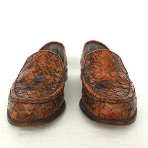 May include: A pair of brown leather woven loafers. The loafers have a pointed toe and a slip-on design.