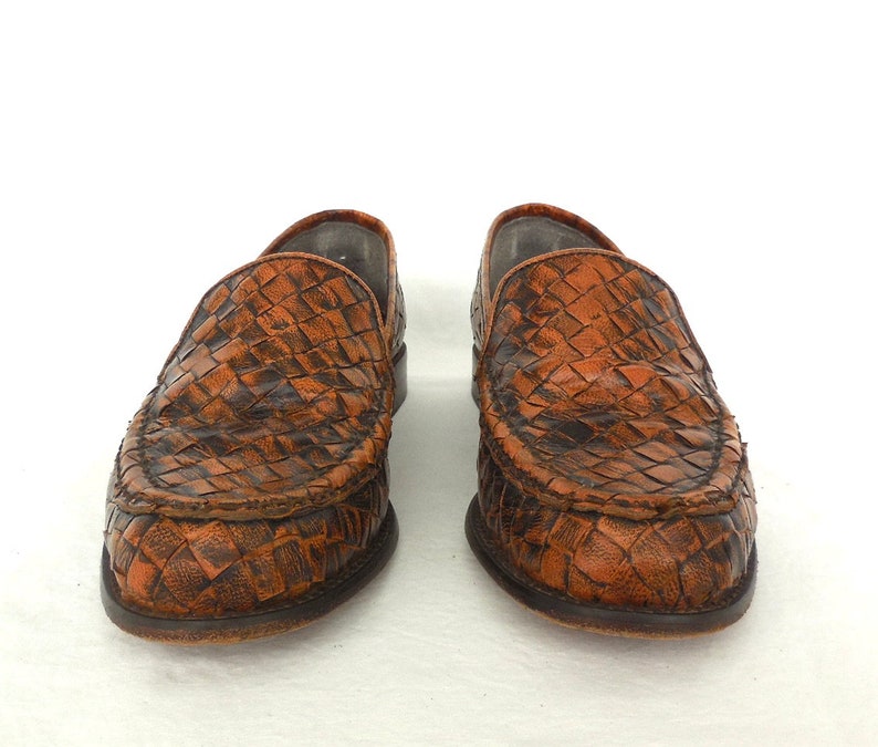 May include: A pair of brown leather woven loafers. The loafers have a pointed toe and a slip-on design.