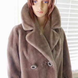 May include: A long-sleeved, brown faux fur coat with a large collar and double-breasted closure. The coat has two large buttons with a silver trim.