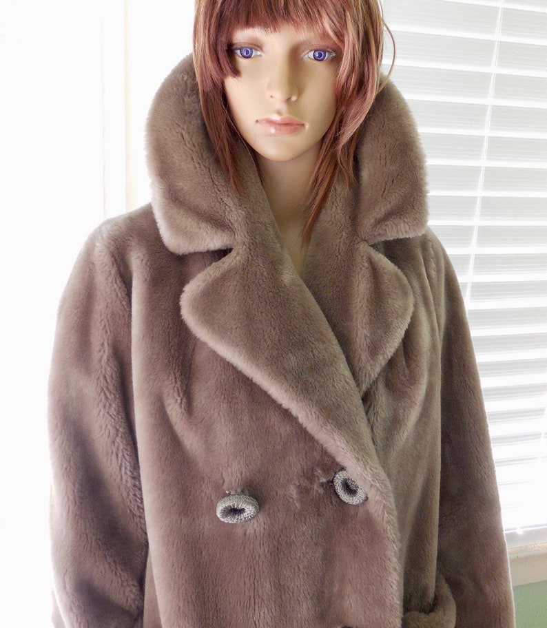 May include: A long-sleeved, brown faux fur coat with a large collar and double-breasted closure. The coat has two large buttons with a silver trim.