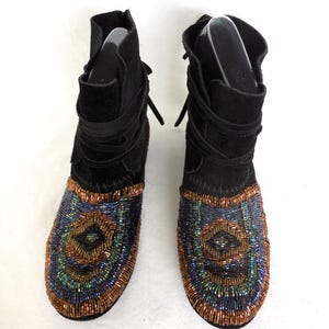 K&ouml;nnte beinhalten: Schwarze Wildleder-Ankle Boots mit aufwendigen Perlenmustern auf der Zehenpartie. Die Perlenarbeiten zeigen ein Muster aus konzentrischen Kreisen in Blau-, Gr&uuml;n- und Kupfert&ouml;nen. Die Stiefel haben einen Wickelriemen und einen umgeschlagenen Schaft.