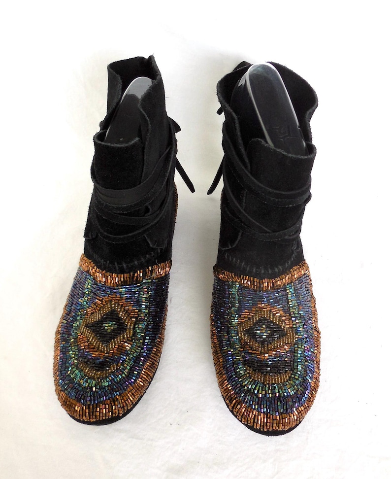 K&ouml;nnte beinhalten: Schwarze Wildleder-Ankle Boots mit aufwendigen Perlenmustern auf der Zehenpartie. Die Perlenarbeiten zeigen ein Muster aus konzentrischen Kreisen in Blau-, Gr&uuml;n- und Kupfert&ouml;nen. Die Stiefel haben einen Wickelriemen und einen umgeschlagenen Schaft.