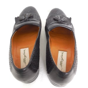 May include: A pair of black leather loafers with a woven pattern and tassel detail. The loafers have a brown leather insole with the brand name "Meglan" printed on them.