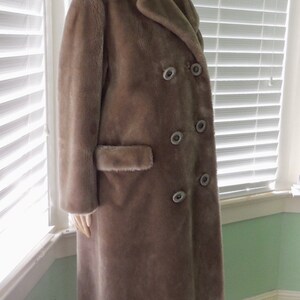 May include: A long, gray faux fur coat with a double-breasted closure and large buttons. The coat has a large collar and a pocket on the left side.