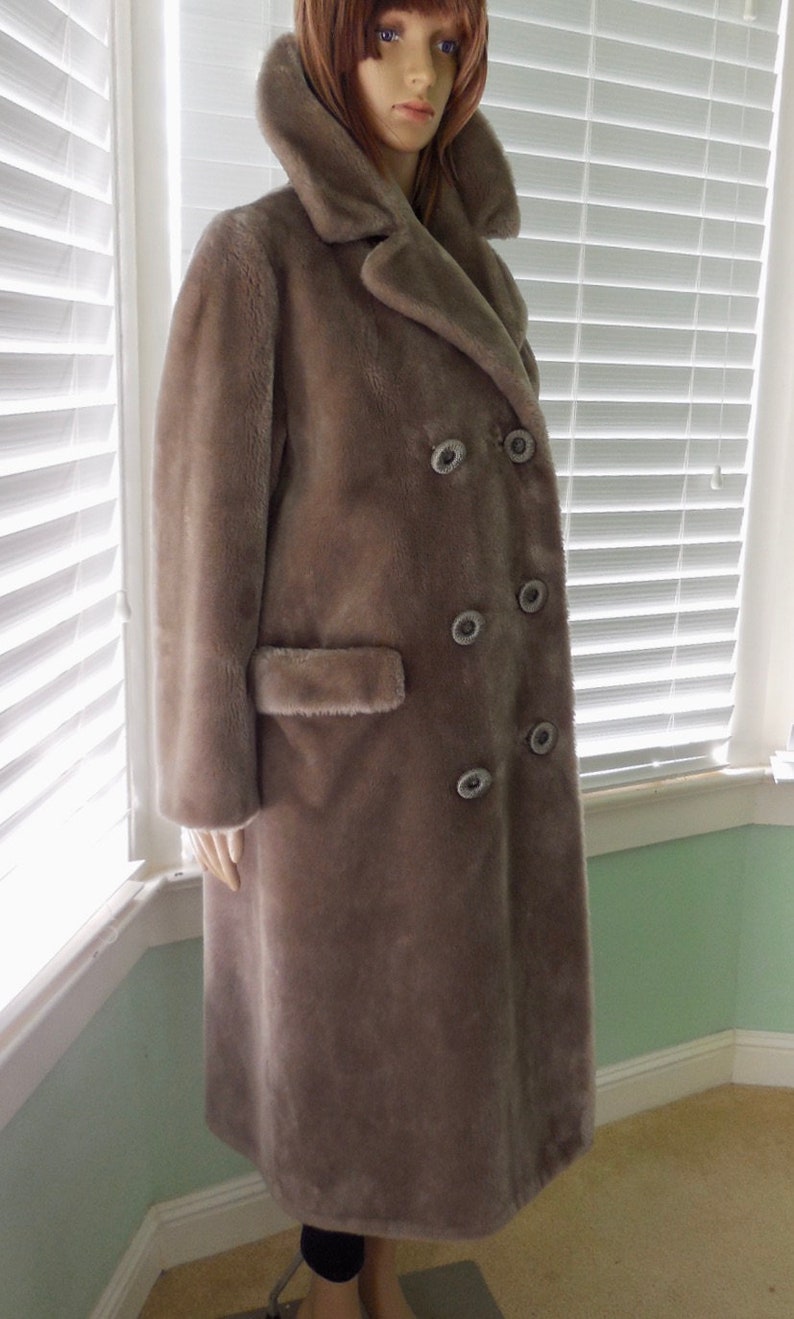 May include: A long, gray faux fur coat with a double-breasted closure and large buttons. The coat has a large collar and a pocket on the left side.