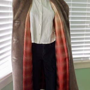 May include: A long, gray faux fur coat with a red and white striped satin lining. The coat has a hood and a button closure.