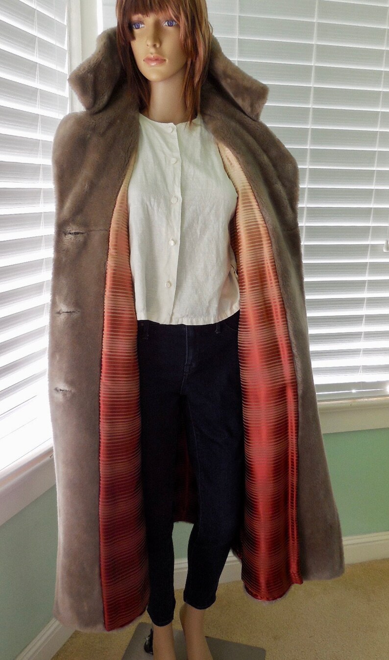 May include: A long, gray faux fur coat with a red and white striped satin lining. The coat has a hood and a button closure.