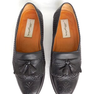 May include: A pair of black leather tassel loafers with a woven pattern and a perforated design. The loafers have the brand name "Merry-Go-Round" printed on the insole.