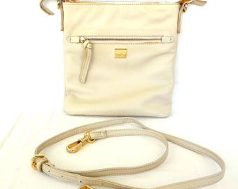 May include: Cream-colored leather crossbody bag with a gold zipper and hardware. The bag has a rectangular shape with a front zipper pocket and a long, adjustable strap. The bag is shown on a white background.