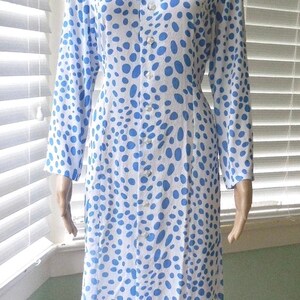 May include: A white dress with a blue polka dot pattern. The dress features long sleeves, a collared neckline, and a button-down front. The dress is knee-length and has a fitted shape.