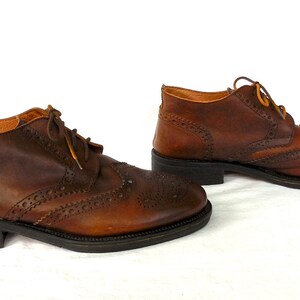 Pode incluir: Um par de botas de tornozelo de couro marrom com detalhes de brogue e fecho de cadar&ccedil;o.