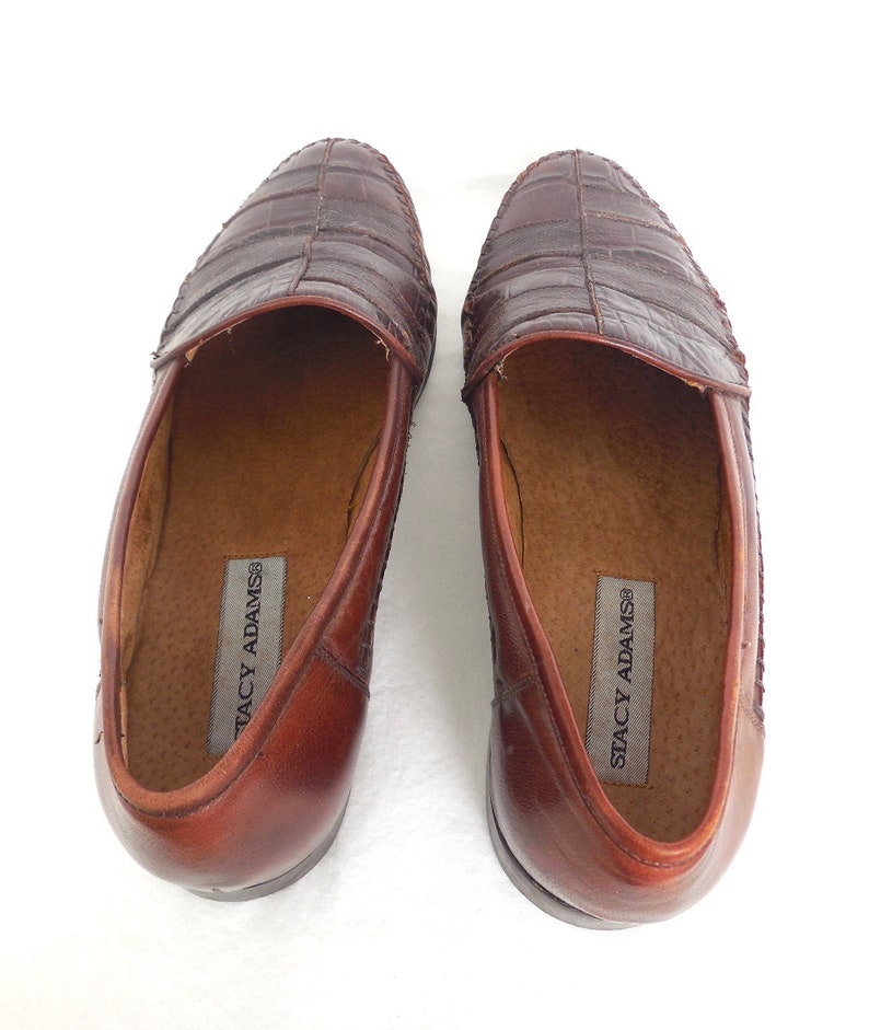 K&ouml;nnte beinhalten: Ein Paar braune Lederschuhe mit Kroko-Pr&auml;gung. Die Loafer sind slip-on und tragen den Markennamen "Stacy Adams" auf der Innensohle.