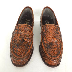 May include: A pair of brown leather woven loafers with the text "Joan Handmade" on the inside of each shoe.