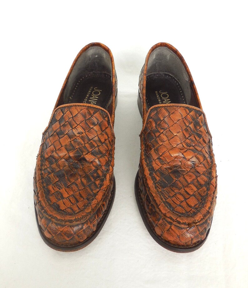 May include: A pair of brown leather woven loafers with the text "Joan Handmade" on the inside of each shoe.