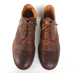 Pode incluir: Um par de botas de couro marrom com brogues, costuras e perfura&ccedil;&otilde;es decorativas. As botas t&ecirc;m cadar&ccedil;os e uma ponta arredondada.