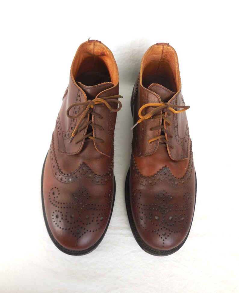 Pode incluir: Um par de botas de couro marrom com brogues, costuras e perfura&ccedil;&otilde;es decorativas. As botas t&ecirc;m cadar&ccedil;os e uma ponta arredondada.