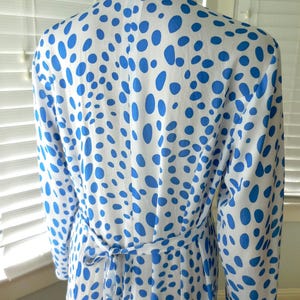 May include: White dress with a blue polka dot pattern. The dress has long sleeves, a collar, and a tie belt at the waist. The dress is made of a lightweight fabric.