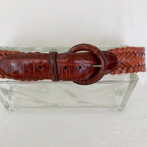 May include: A brown leather belt with a braided design and a round buckle.