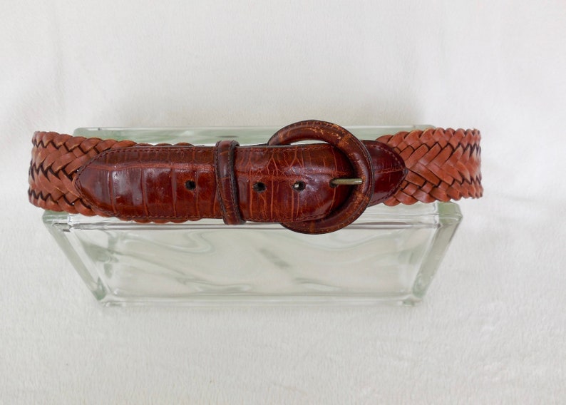 May include: A brown leather belt with a braided design and a round buckle.