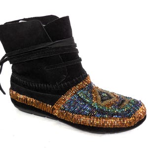 K&ouml;nnte beinhalten: Schwarzer Wildleder-Kn&ouml;chelstiefel mit Perlenmuster. Der Stiefel hat einen umlaufenden Riemen und ein Perlenmuster in Gold-, Blau- und Gr&uuml;nt&ouml;nen. Die Sohle ist schwarz.