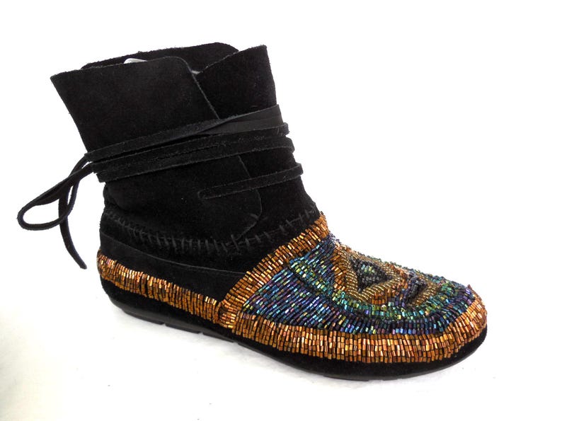 K&ouml;nnte beinhalten: Schwarzer Wildleder-Kn&ouml;chelstiefel mit Perlenmuster. Der Stiefel hat einen umlaufenden Riemen und ein Perlenmuster in Gold-, Blau- und Gr&uuml;nt&ouml;nen. Die Sohle ist schwarz.