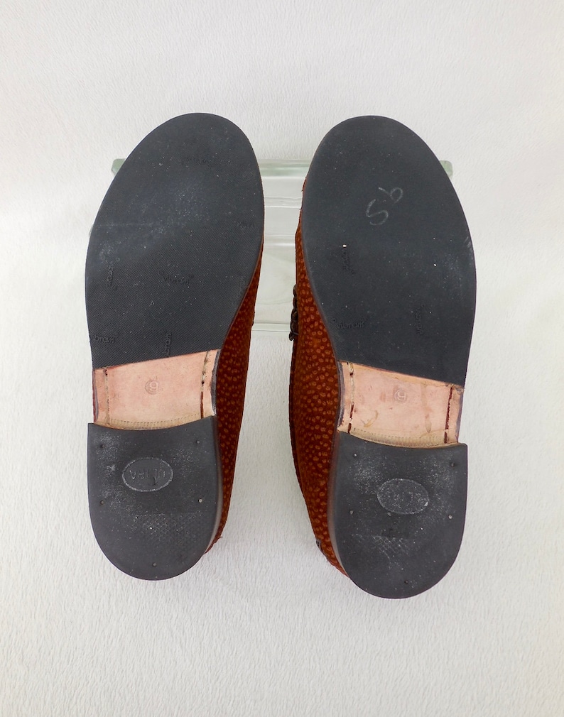 May include: A pair of brown loafers with textured uppers and black rubber outsoles. The soles feature a Vibram logo, a tan leather heel section with the number 9 stamped on it, and a black heel cap with an oval logo and small circular indentations.