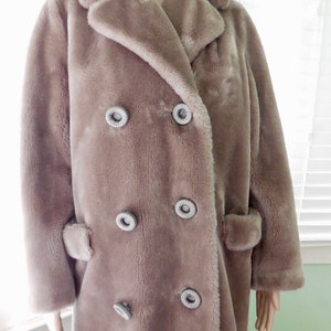 May include: A long, double-breasted faux fur coat in a light brown color. The coat has large, decorative buttons with a silver finish.