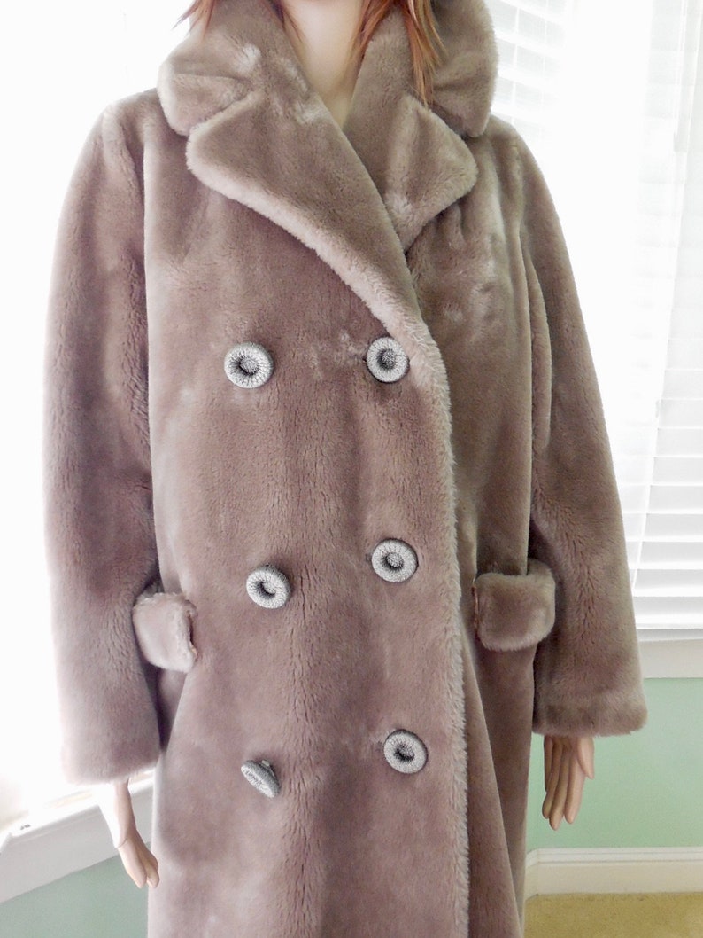 May include: A long, double-breasted faux fur coat in a light brown color. The coat has large, decorative buttons with a silver finish.