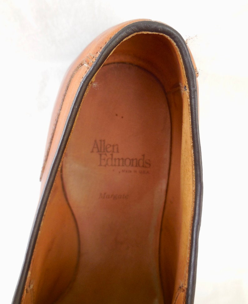 May include: Close-up of a tan leather shoe interior with the brand name "Allen Edmonds" and the style name "Margate" visible. The shoe has a dark brown trim around the opening.