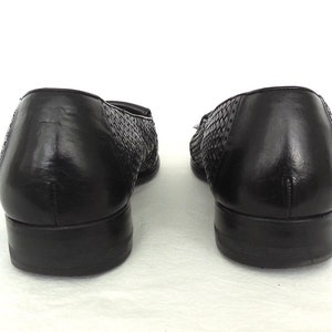 May include: A pair of black leather woven loafers with a low heel. The shoes have a woven pattern on the upper and a smooth leather finish on the back.