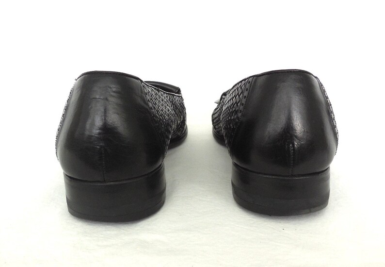 May include: A pair of black leather woven loafers with a low heel. The shoes have a woven pattern on the upper and a smooth leather finish on the back.