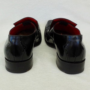 Puede incluir: Un par de zapatos de vestir de cuero negro con dise&ntilde;o de punta de ala. Los zapatos tienen un forro de cuero rojo y una suela de goma negra.