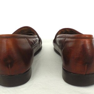K&ouml;nnte beinhalten: Ein Paar braune Leder-Slipper mit einem gewebten Muster auf dem Spann. Die Slipper haben eine abgerundete Spitze und einen niedrigen Absatz.