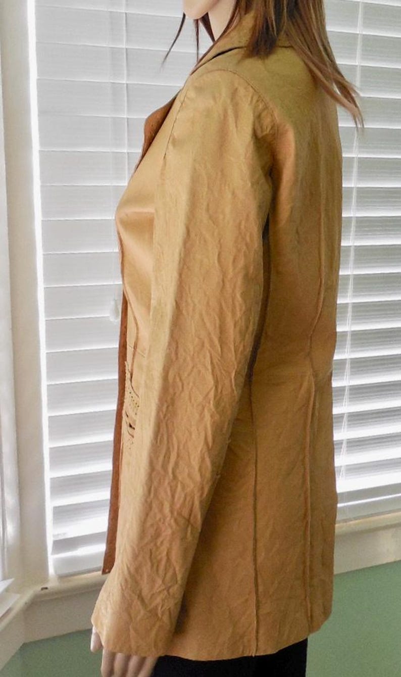 May include: A tan leather jacket with a long, fitted silhouette and a collar. The jacket has a textured surface and a subtle sheen.