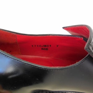 Puede incluir: Primer plano del interior de un zapato de cuero negro con forro rojo. El zapato de talla 7 est&aacute; etiquetado como "1710JW01" y "MIE".