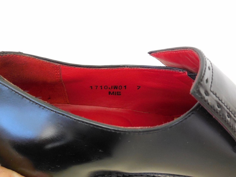Puede incluir: Primer plano del interior de un zapato de cuero negro con forro rojo. El zapato de talla 7 est&aacute; etiquetado como "1710JW01" y "MIE".