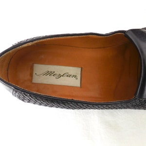 May include: Black leather loafers with a woven pattern and a brown leather insole. The insole has the brand name "Mezlan" printed on it.