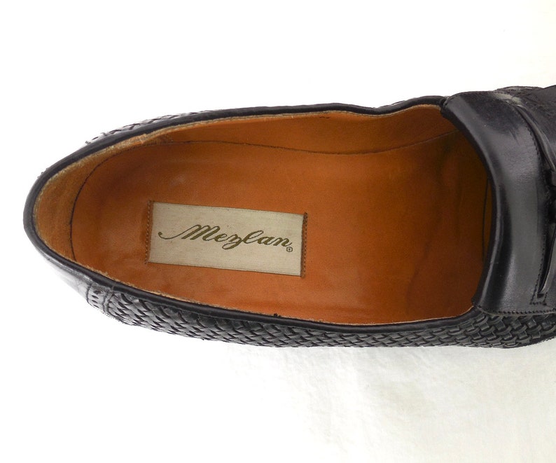 May include: Black leather loafers with a woven pattern and a brown leather insole. The insole has the brand name "Mezlan" printed on it.