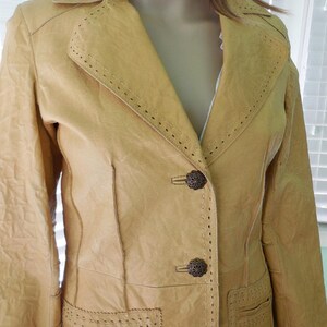 May include: A long, tan leather jacket with decorative stitching and metal buttons. The jacket has a notched collar and a single-breasted closure.