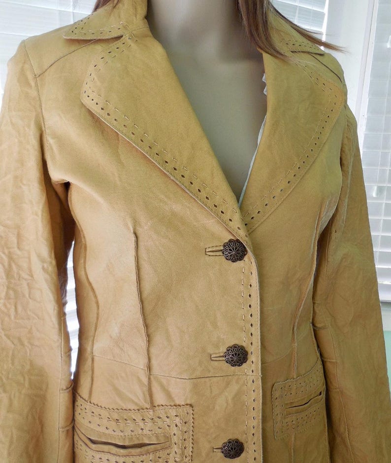 May include: A long, tan leather jacket with decorative stitching and metal buttons. The jacket has a notched collar and a single-breasted closure.
