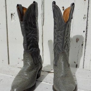 May include: A pair of gray cowboy boots with a textured finish on the lower part and smooth leather on the upper shaft. The boots have a pointed toe and a stacked heel, showcasing classic Western wear.