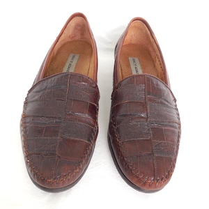 K&ouml;nnte beinhalten: Ein Paar braune Lederschuhe mit Kroko-Pr&auml;gung. Die Loafer haben einen gen&auml;hten Rand und ein Slip-On-Design. Der Markenname "Stacy Adams" ist auf der Innenseite der Schuhe sichtbar.