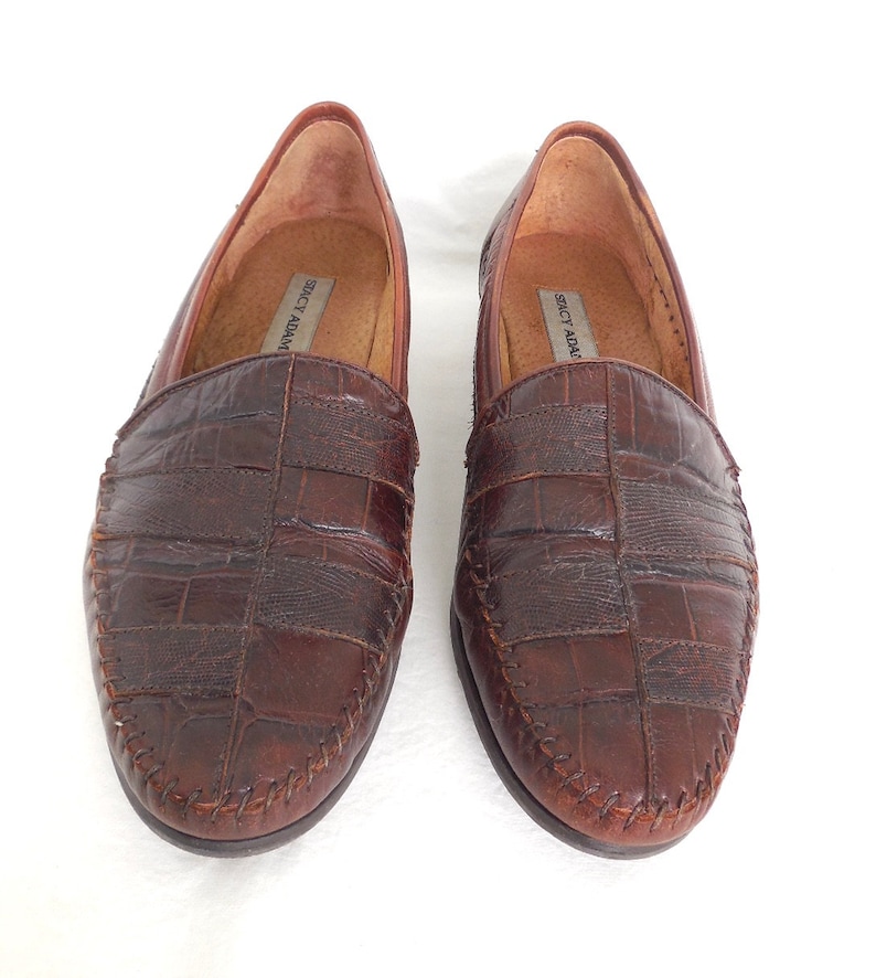 K&ouml;nnte beinhalten: Ein Paar braune Lederschuhe mit Kroko-Pr&auml;gung. Die Loafer haben einen gen&auml;hten Rand und ein Slip-On-Design. Der Markenname "Stacy Adams" ist auf der Innenseite der Schuhe sichtbar.