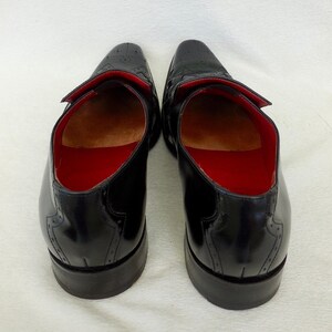 Puede incluir: Un par de zapatos de cuero negro con dise&ntilde;o de punta de ala y forro rojo. Los zapatos tienen la punta cerrada y un cierre de cordones.