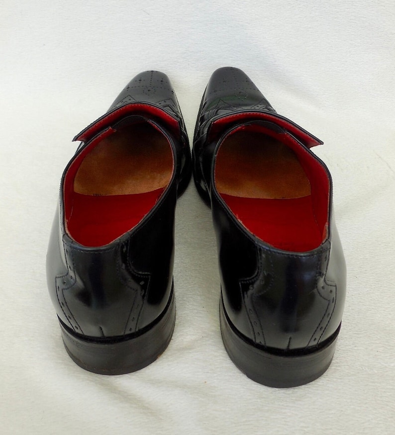 Puede incluir: Un par de zapatos de cuero negro con dise&ntilde;o de punta de ala y forro rojo. Los zapatos tienen la punta cerrada y un cierre de cordones.
